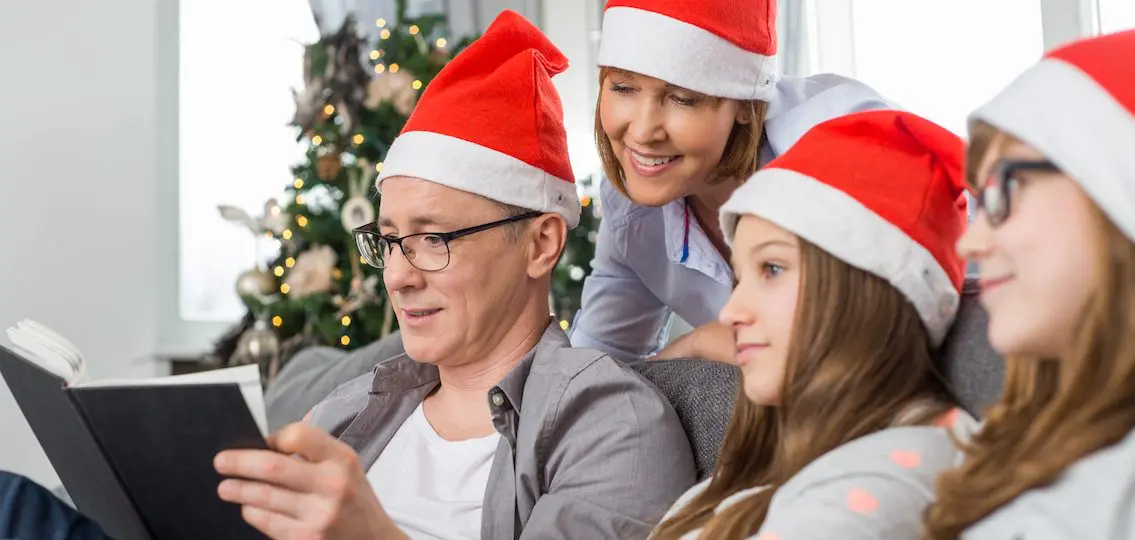 Father reading book for family at home during Christmas all wearing santa hats