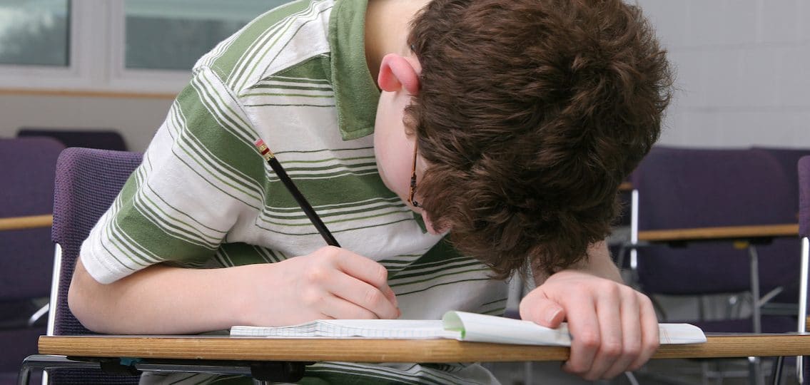 teenager hunched over doing homework with his face really close to the paper