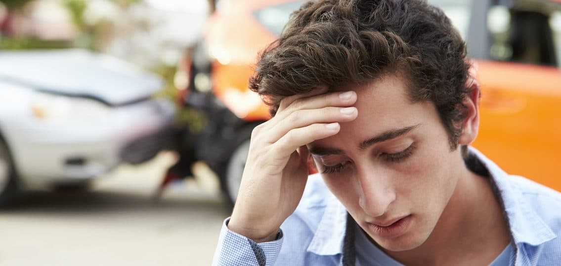 Teen after car crash looking upset with blurred car accident in the background