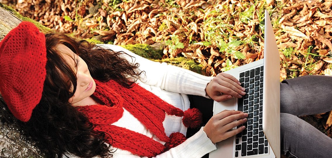 Beauty gorgeous autumn girl sitting in nature beside the tree and working on laptop