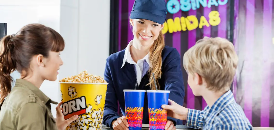Brother and sister buying popcorn from teen girl working at concession stand in cinema