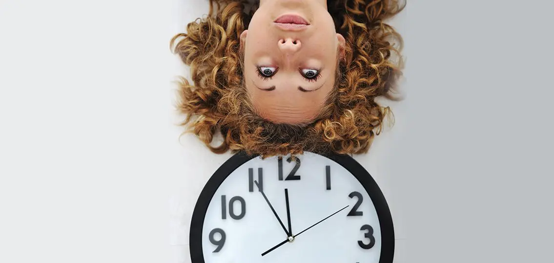 Girl upside down looking at clock impatiently
