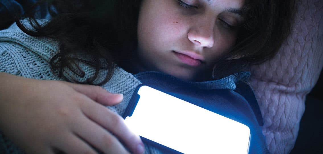 teen Girl Fast Asleep With Her Phone glowing On Her Chest