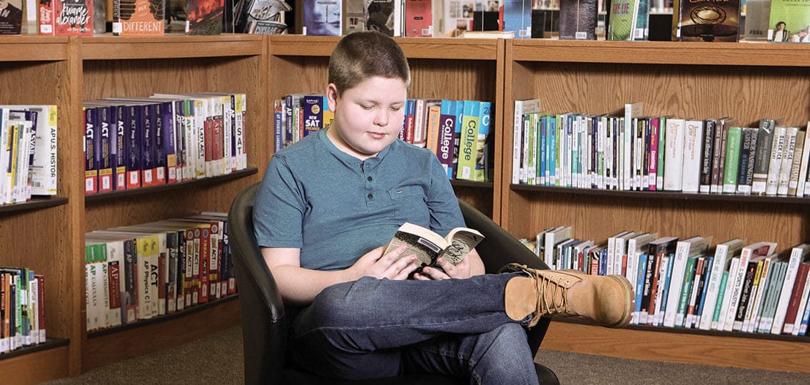 young teen boy reading in the library