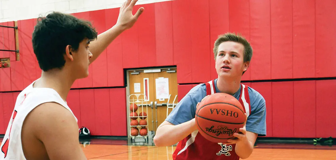 teen boys playing basketball in a red school gym