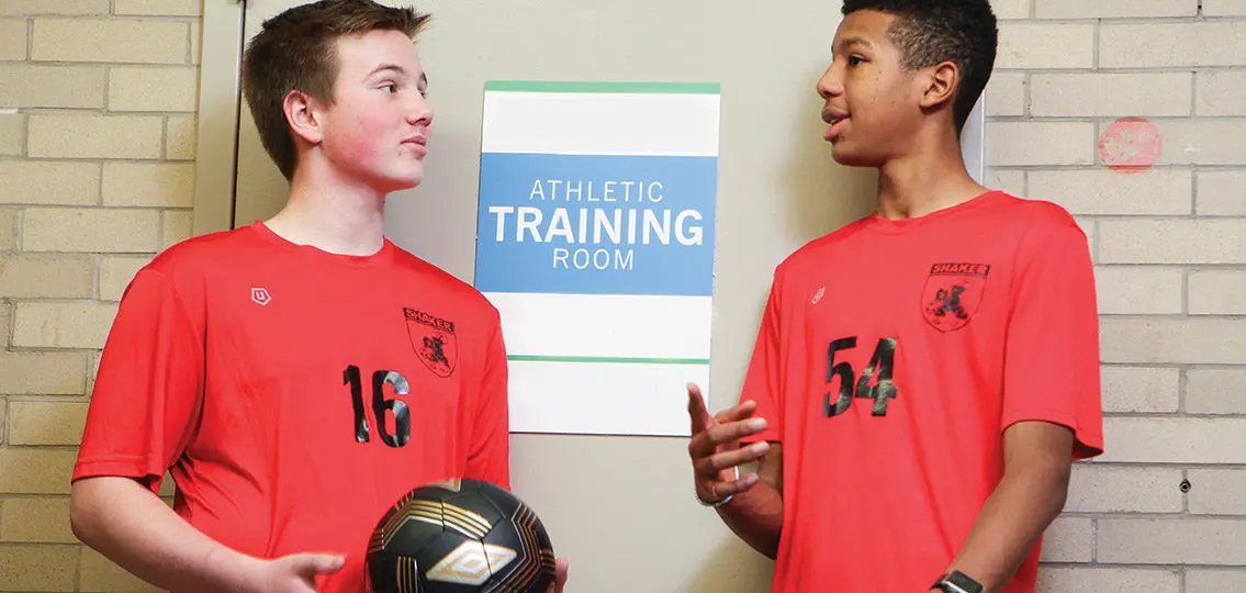 two teen soccer players chatting in room labeled athletic training room