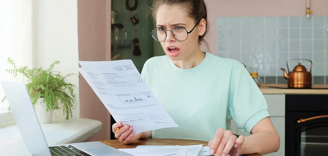 Indoor Closeup Of Young Emotional European Lady Dealing With Sheets Of Paper And Bills At Home Having Opened Mouth As If She Can Not Believe These Big Numbers To Pay Are True, Feeling Despair
