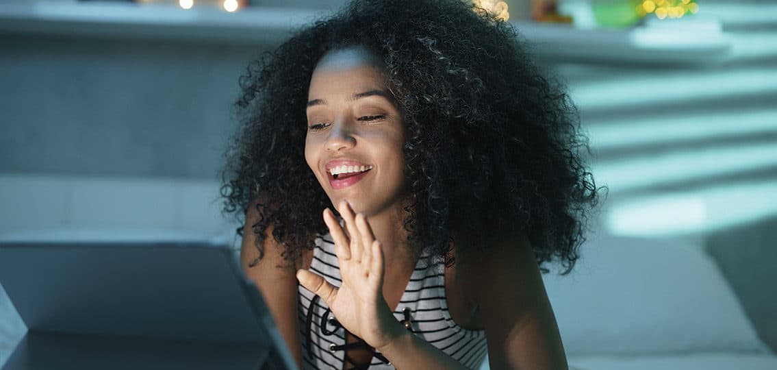 Happy african american teen in bed at home with her laptop. Young black woman using computer webcam for a video chat at night.