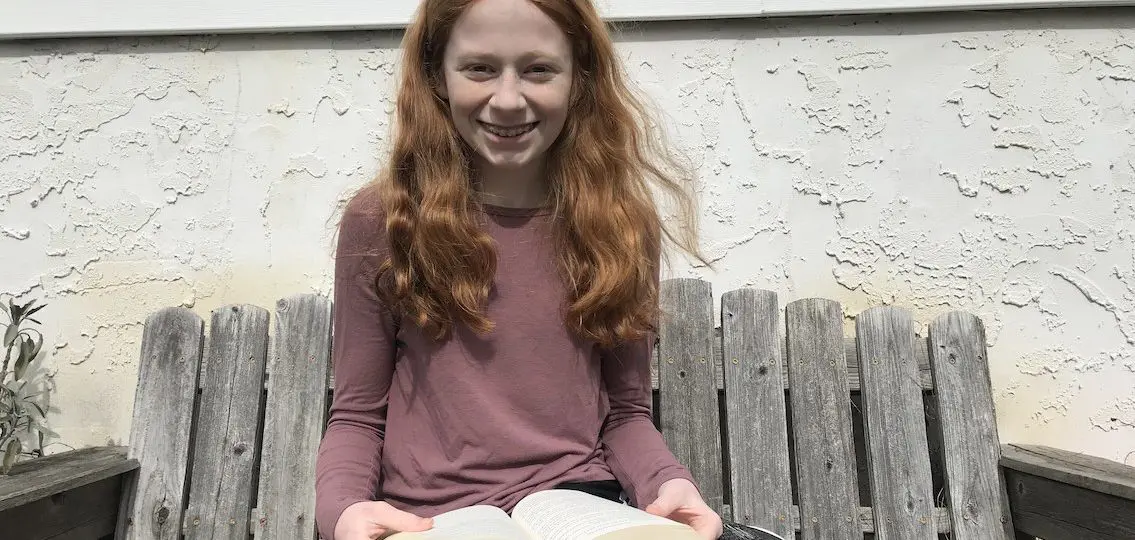 Eighth grade girl smiling reading a book outside