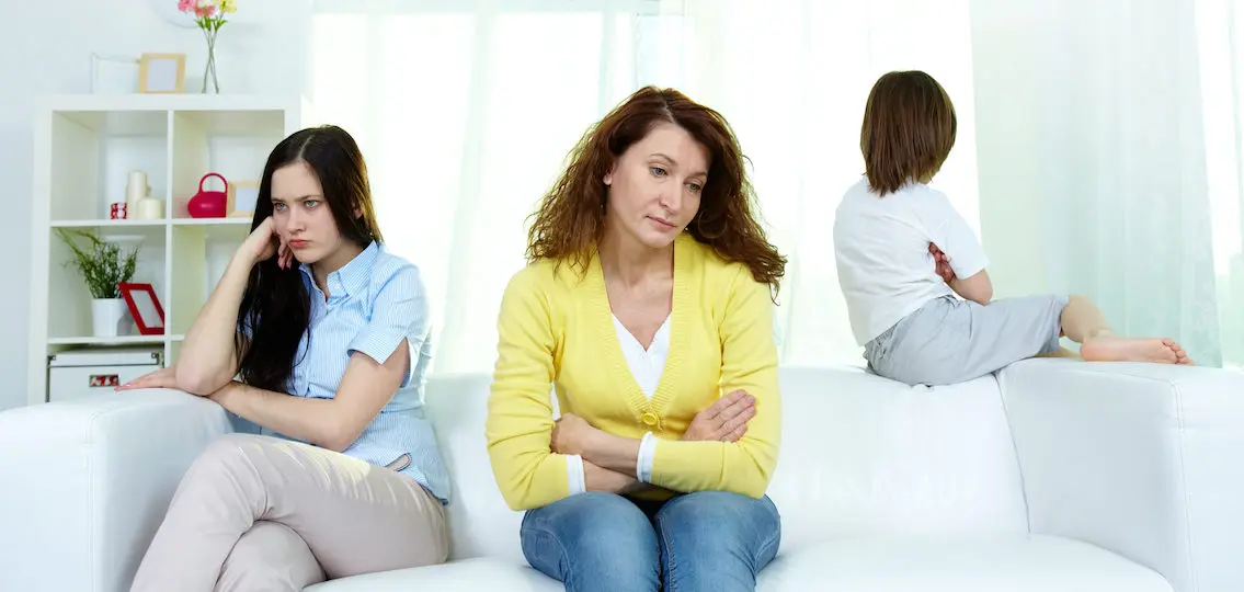 Photo of sad woman and her teenage daughter sitting on sofa during argument with little boy near by, parenting mistakes fallout