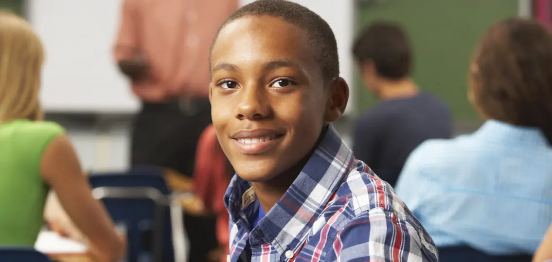 teen boy smiling in a classroom blurred background