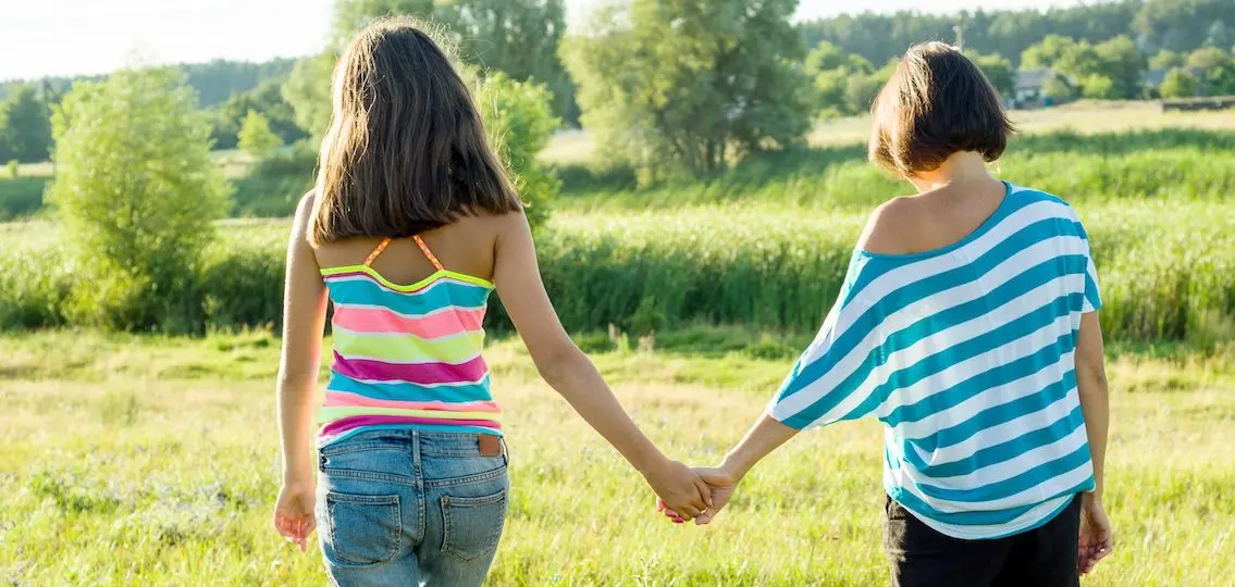Mother and teen daughter holding hands, back view. Photo on nature in a sunny summer day