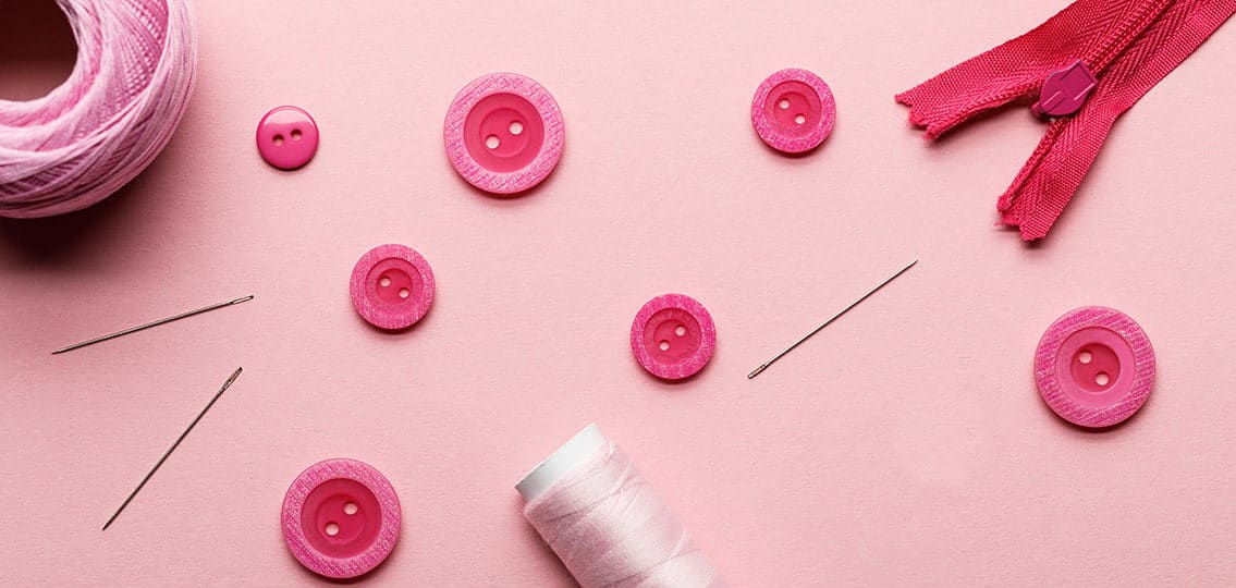 pink buttons on a pink table surrounded by string yarn and a zipper and sewing equipment