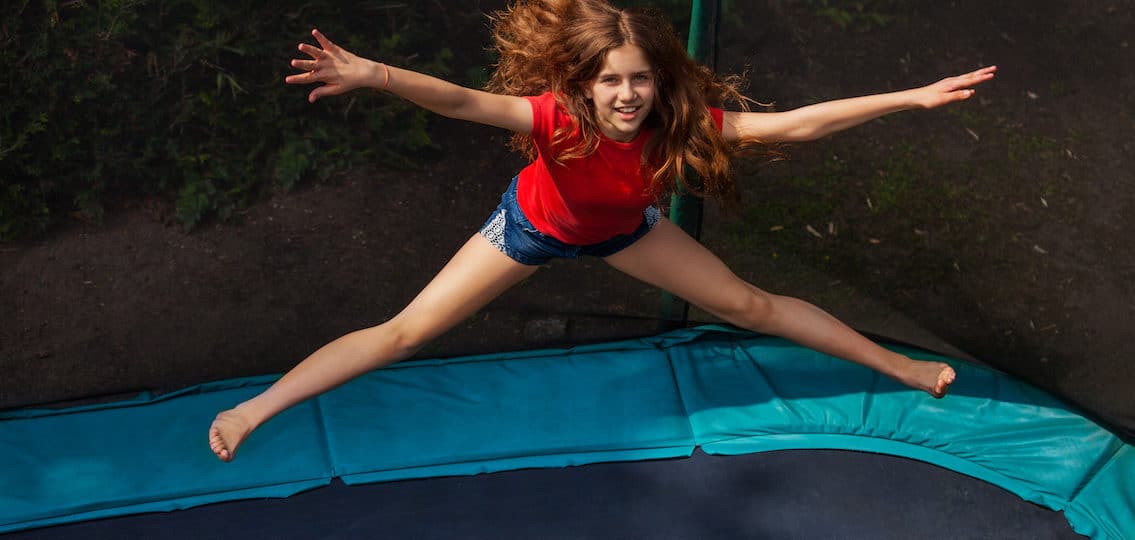 Top view portrait of teenage girl jumping on trampoline with enclosure outdoors