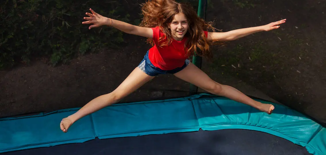 Top view portrait of teenage girl jumping on trampoline with enclosure outdoors