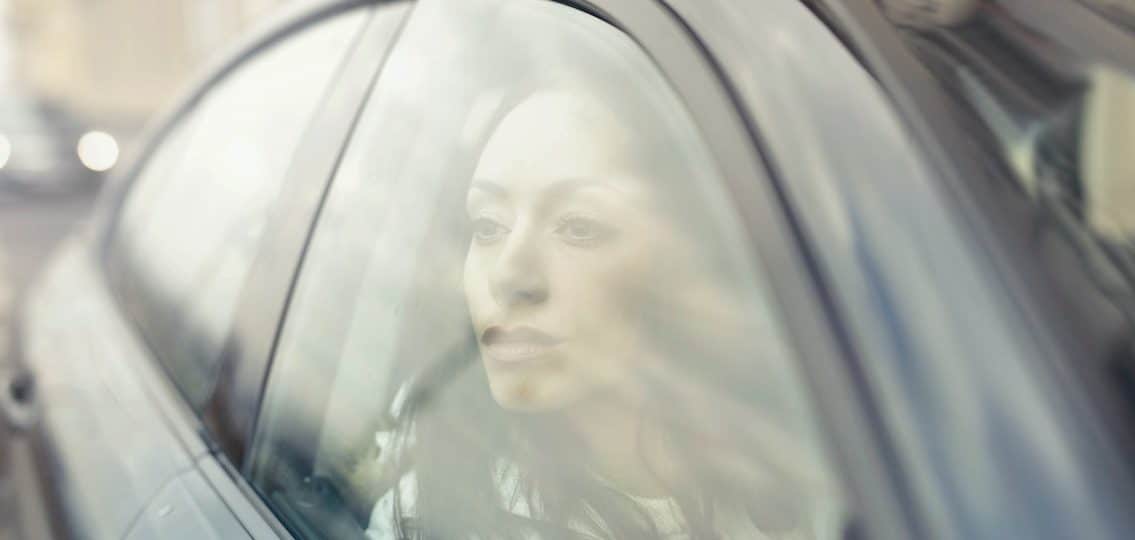 woman looking sadly out the passenger side window of a car, blurred