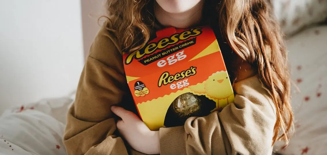 teen girl hugging a reese's peanut butter egg to her chest on a bed close up