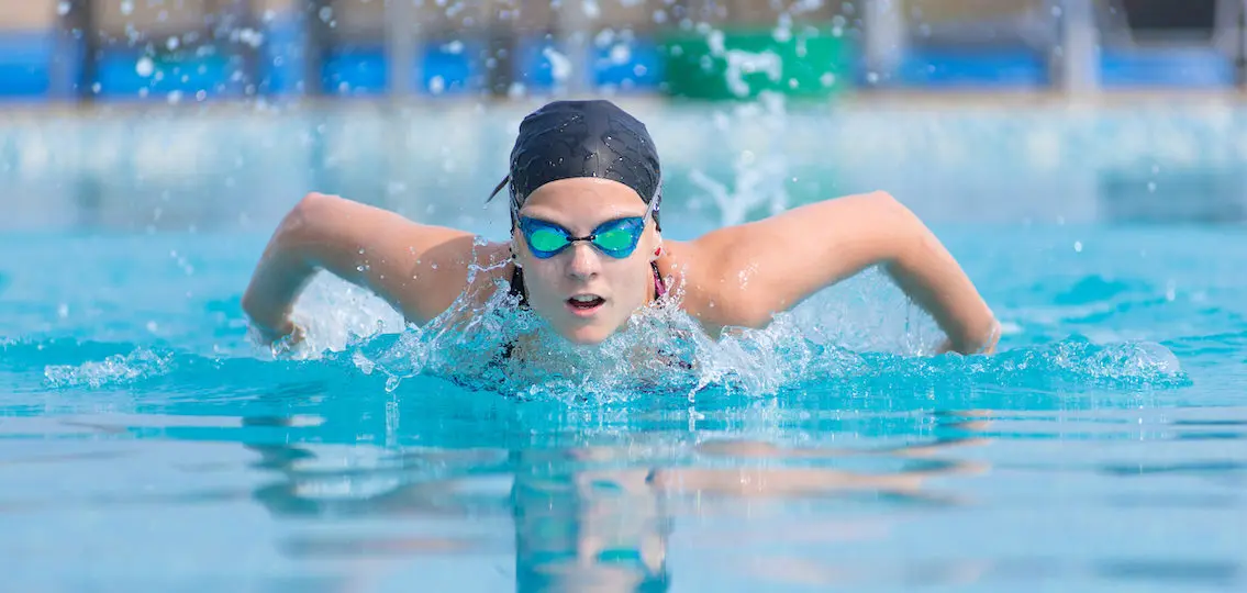 Young teen athlete in goggles and cap swimming butterfly stroke style in the blue water pool