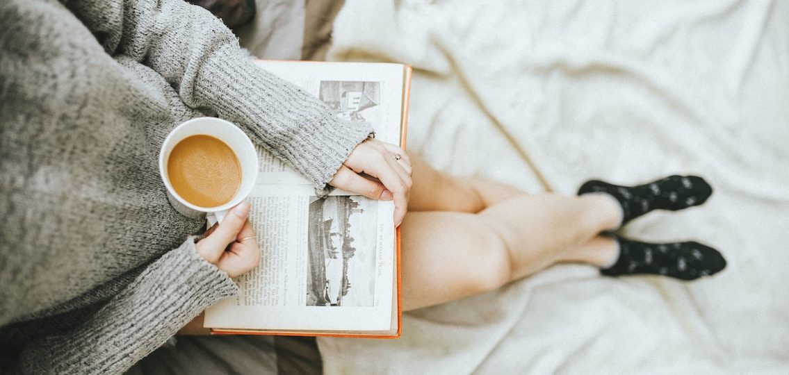 woman reading a book in her bed with a coffee mug