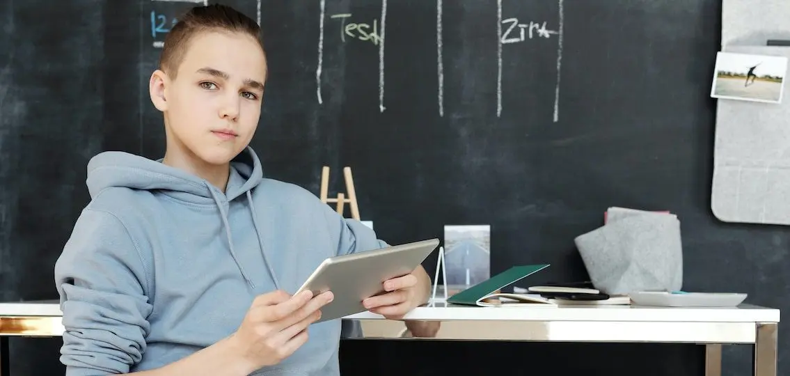 serious teen with ipad in classroom in front of blackboard struggling with common learning problems