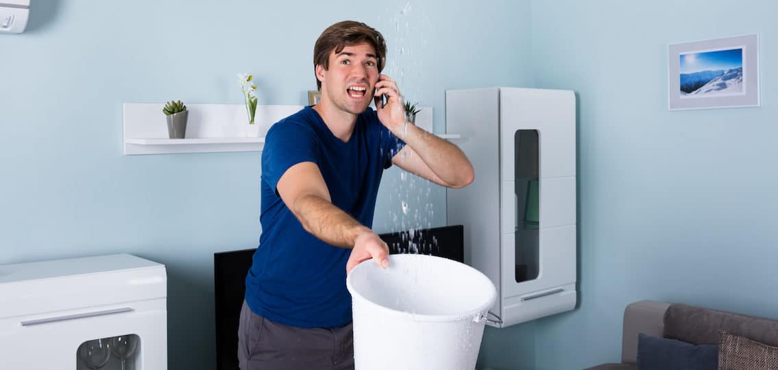 Worried college age man Calling Plumber While Leakage Water Falling Into Bucket At Home