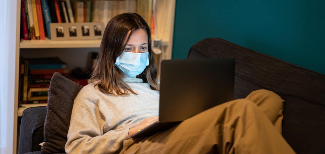 immonucompromised woman on a computer wearing a mask on her couch