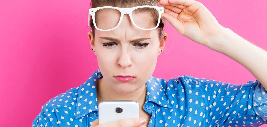 Young woman staring in confusion at her cellphone on a pink background