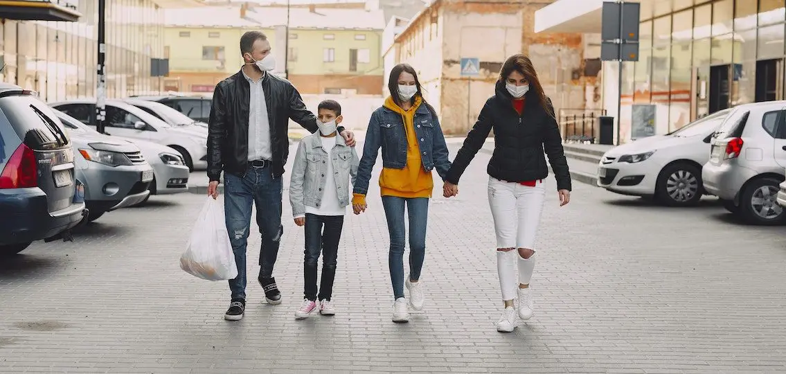 family wearing masks holding hands as they walk through a parking lot