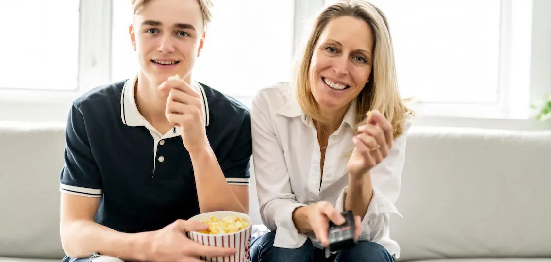 mom and son watching a movie on the couch with a bowl of popcorn