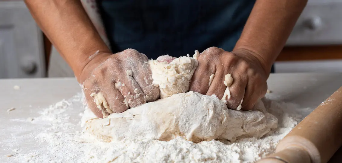 closeup of hands kneading dough on a table covered in flour