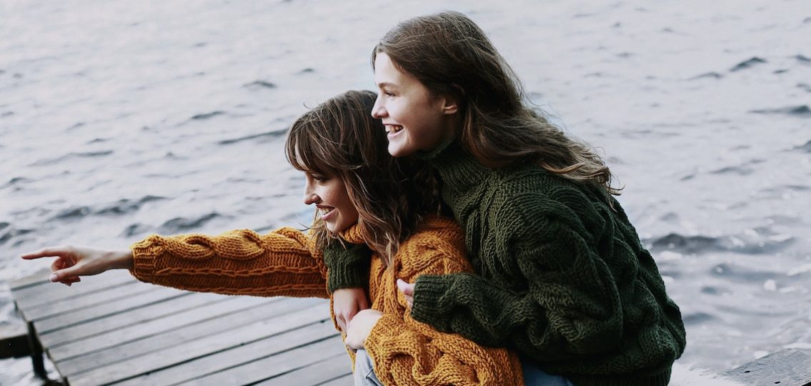 two sisters laughing and hugging on a pier in sweaters