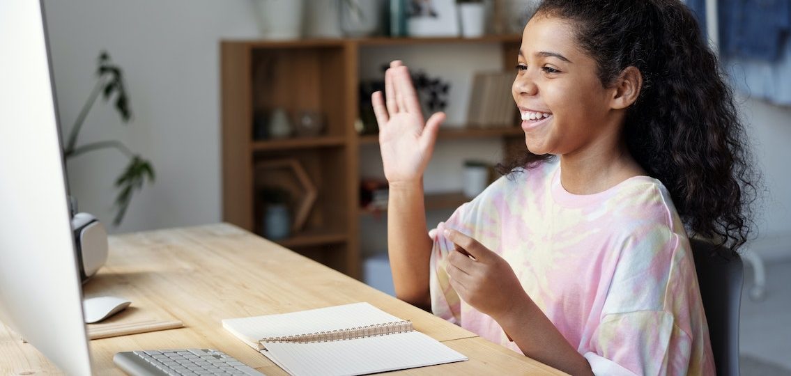 teen girl smiling and waving at the computer with an open notebook