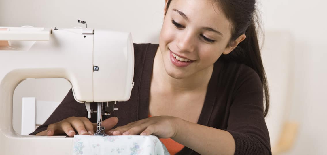 young teen girl learning to sew clothes at home with a sewing machine