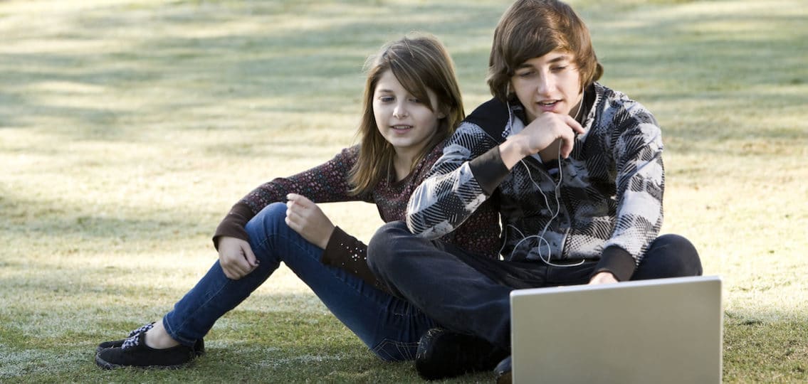 Teen brother and sister hanging out outside and looking at a computer together