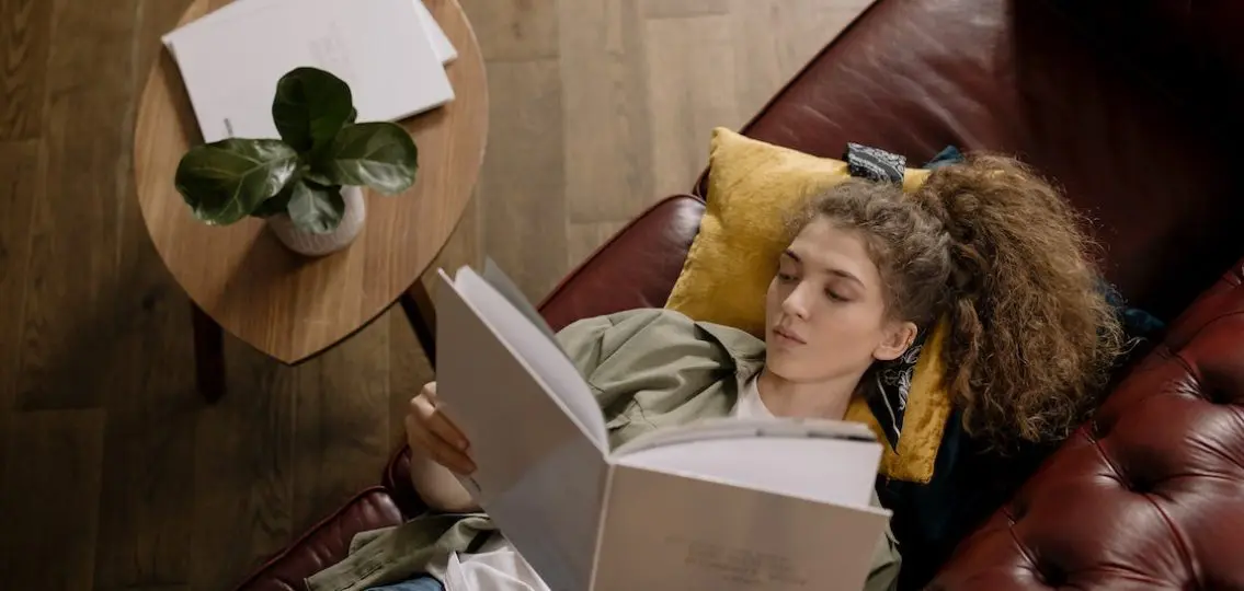 teenage girl reading by herself lying on a couch