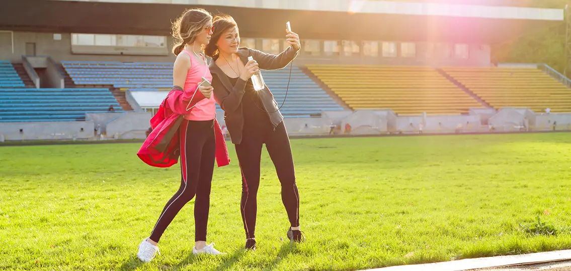 Mother and daughter or two teen girls resting after workout at stadium. Photographed together selfi photo