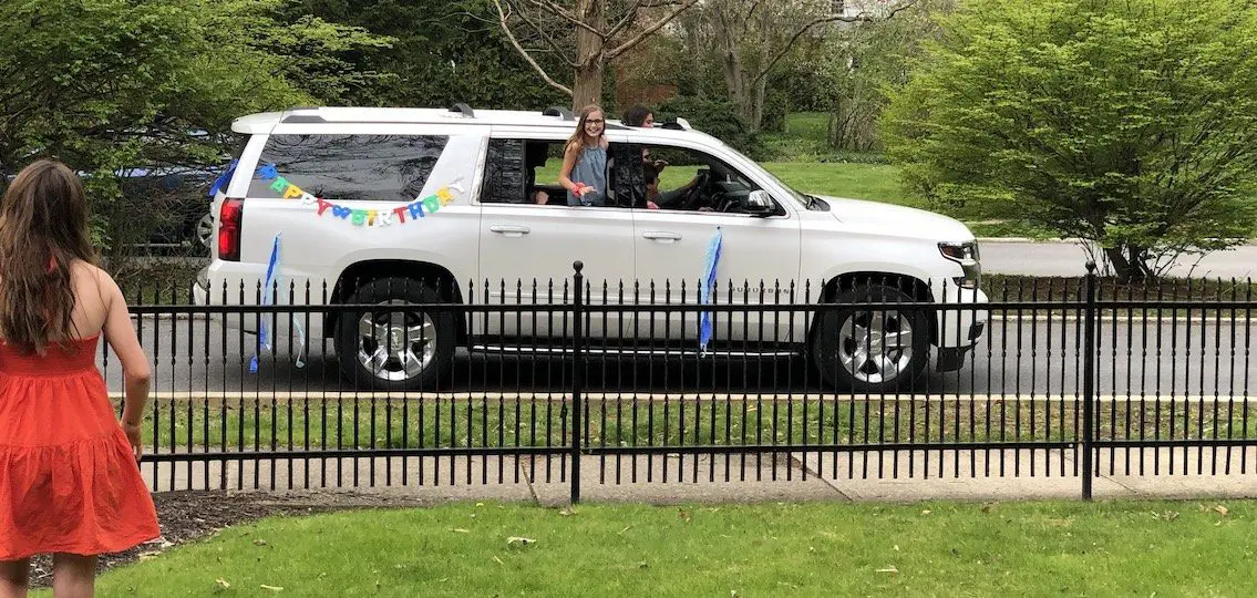 teen leaning out of a car with happy birthday banners on the back toward a girl in a dress