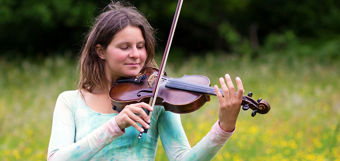 middle school girl playing the violin in a meadow