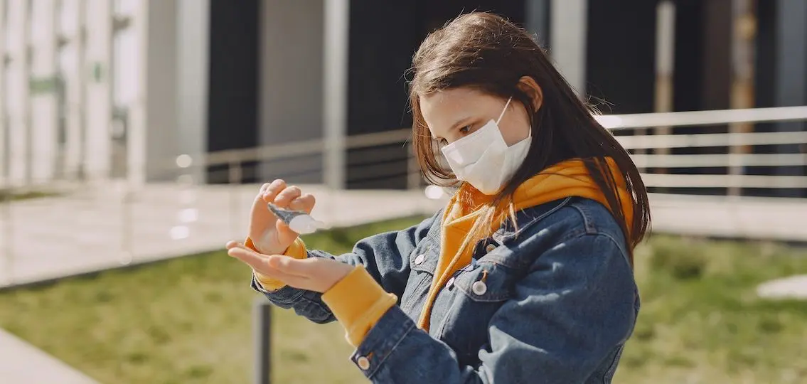 teen girl outside in a mask using hand sanitizer