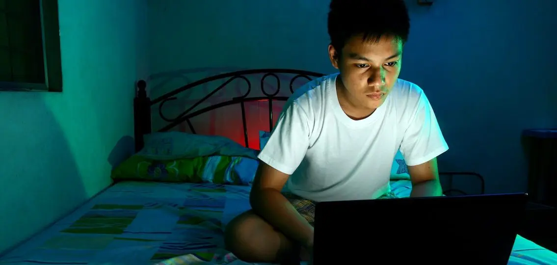 teenage boy on bed at night watching something on his computer