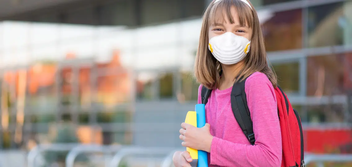 young teen girl with books and backpack at school wearing a mask