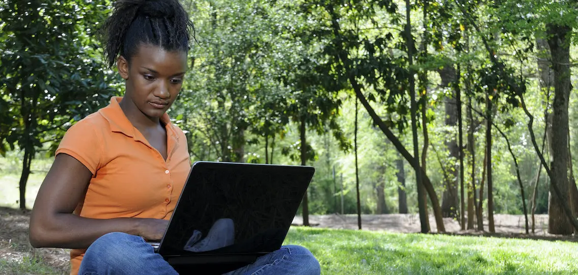 A teenage girl outside on her computer in the woods