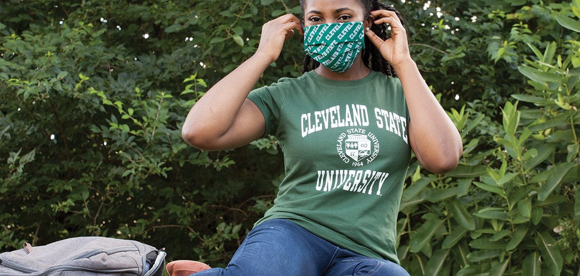 Freshman in a cleveland state university t shirt sitting on campus in a mask