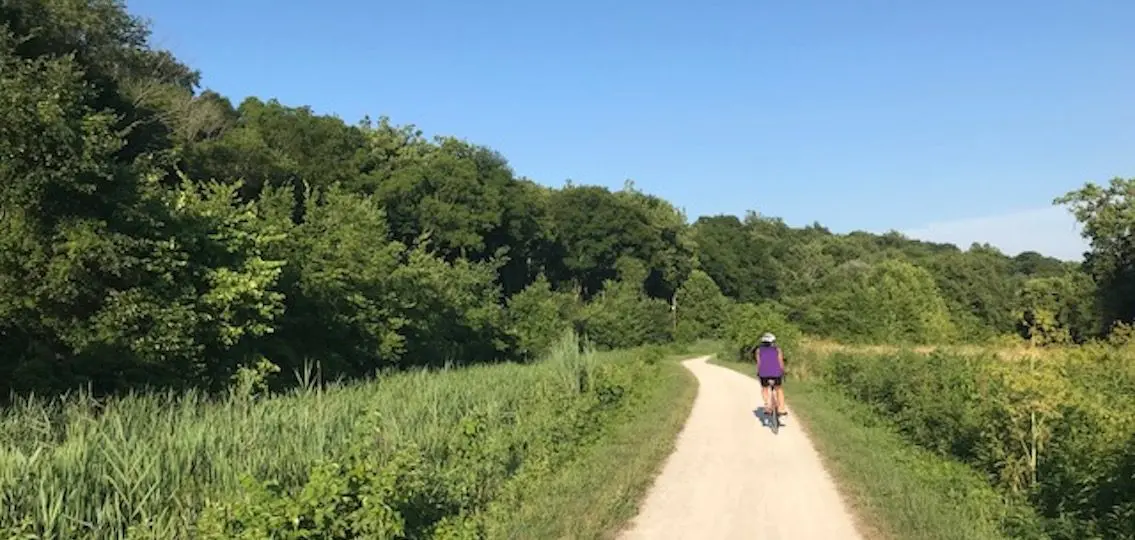 Woman riding a road bike down a dirt path surrounded by greenery