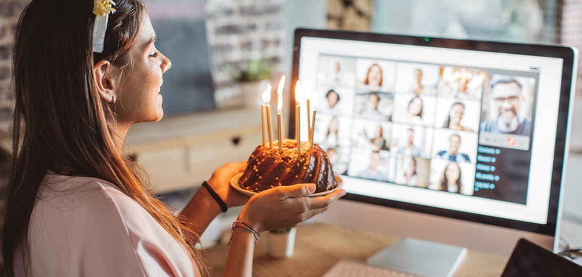 Teenage girl at home during pandemic isolation 18th birthday celebration and have video call with friends. She holding birthday cake with lighted candles