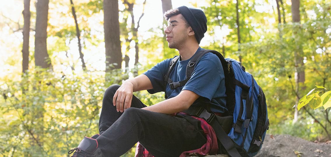 Teenager hiking outside in nature with large backpack