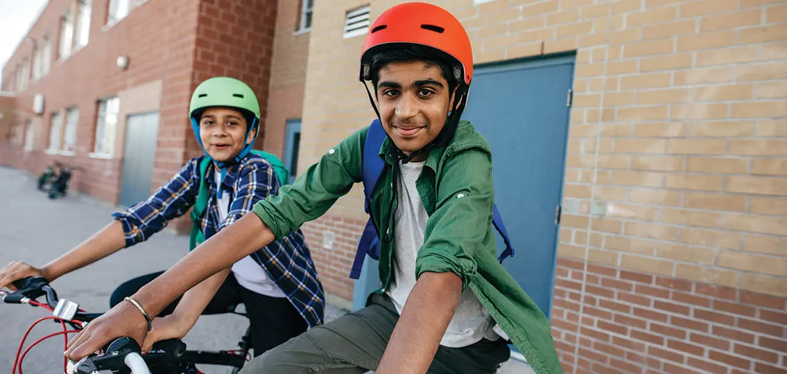 Two middle school boys on bikes outside their school smiling at camera