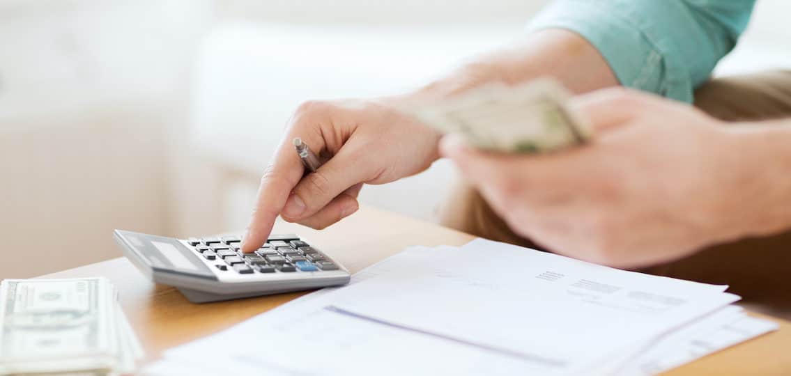 savings, finance class, economy and home concept - close up of man with calculator counting money and making notes at home