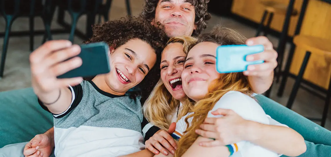 Cheerful family sitting on the sofa and taking a selfie connecting through technology