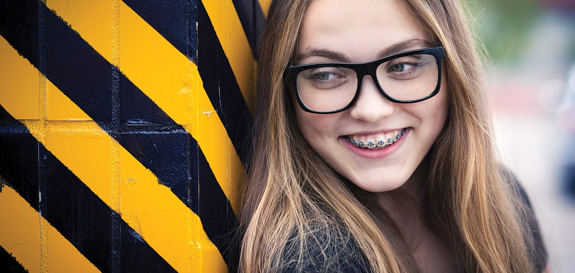 Portrait of smiling teenage girl with braces standing by the black and yellow striped warning wall